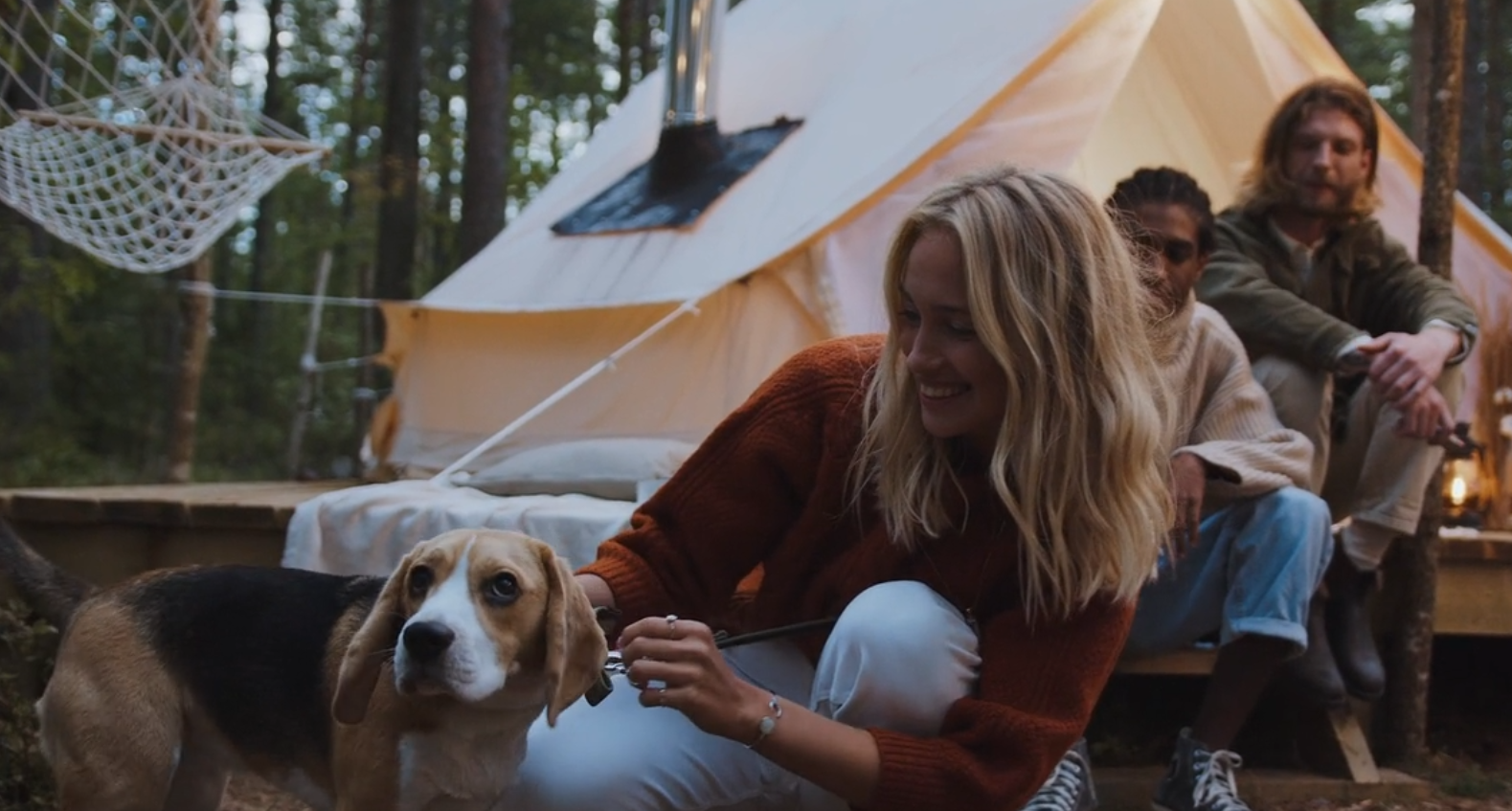 Host greeting guests on a wooden deck outside a glamping tent at sunset