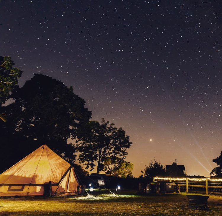 Luxury glamping tent under a starry sky with warm interior lighting and deck chairs